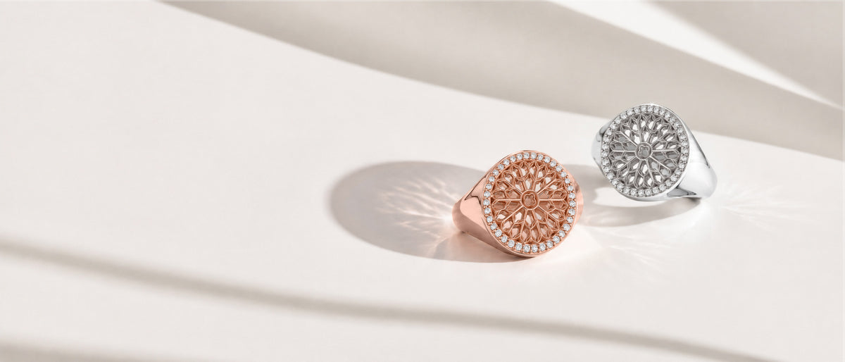 Rose gold and white gold Notre Dame signet rings on a pale surface
